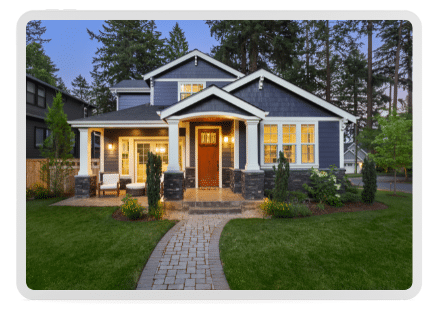 A modern two-story house with a gray exterior, prominent front porch, and a well-maintained lawn is surrounded by tall trees. Perfect for those looking fora roofing and siding replacement to enhance curb appeal.