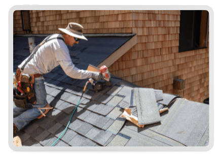 A roofing installer systematically installs an asphalt, engineered roofing shingle from GAF on a mountain home finished in cedar wooden siding