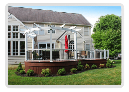 A dark brown composite deck build in with custom curved edge, matching composite base covering and a pergola integrated into the vinyl railing system.