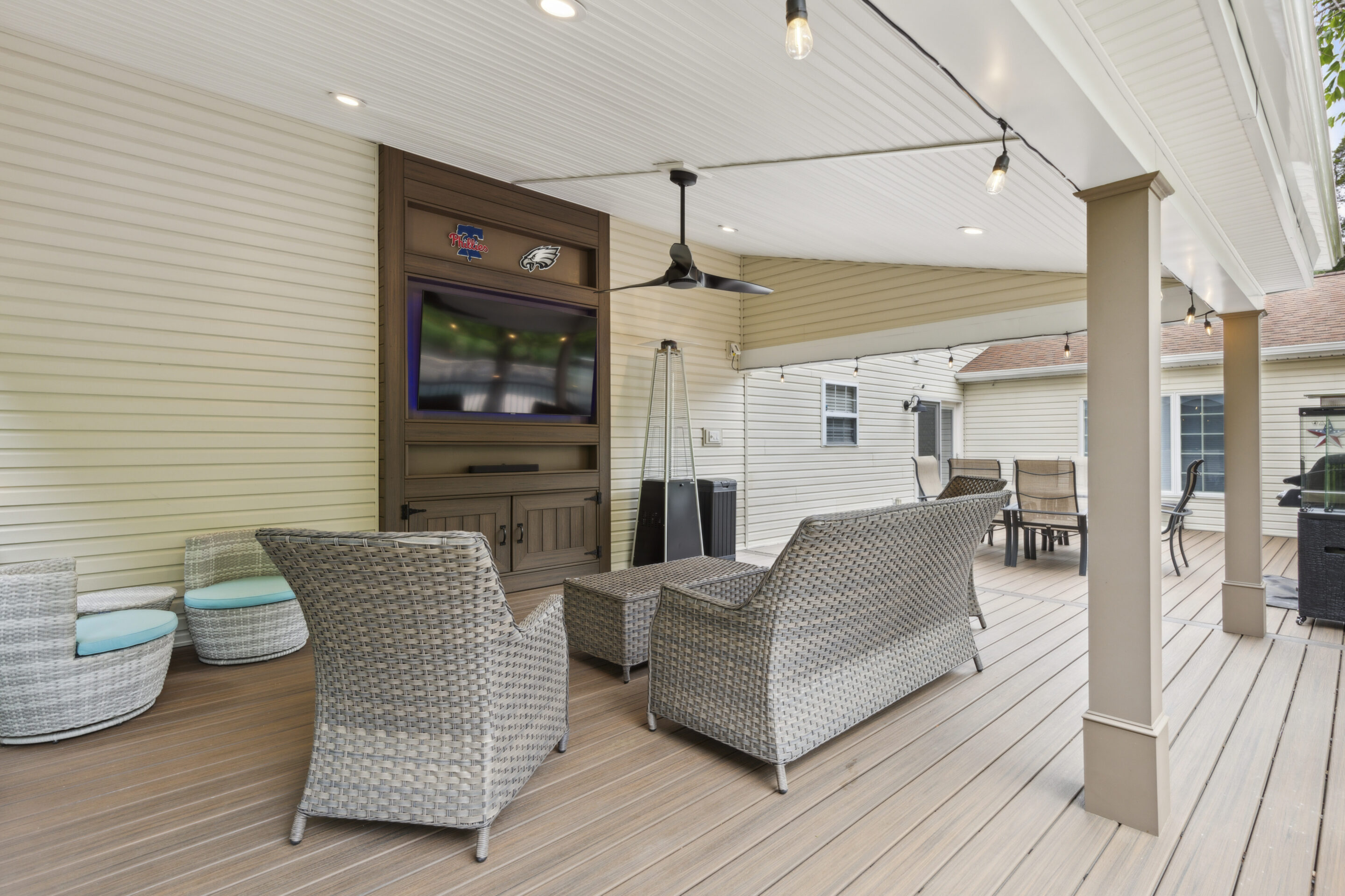 A custom-built deck in Lansdale, PA featuring Trex composite decking, aluminum railings, an A-frame roof covering, a media wall with a mounted TV, built-in lighting, a ceiling fan, and wicker-style outdoor furniture, creating a comfortable outdoor living space 40.2415° N, 75.2838° W